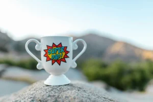 Image of a Trophy-Shaped Mug that Reads Super Dad on a rock with mountains in the background. Image by the RDNE Project via Pexels.com.